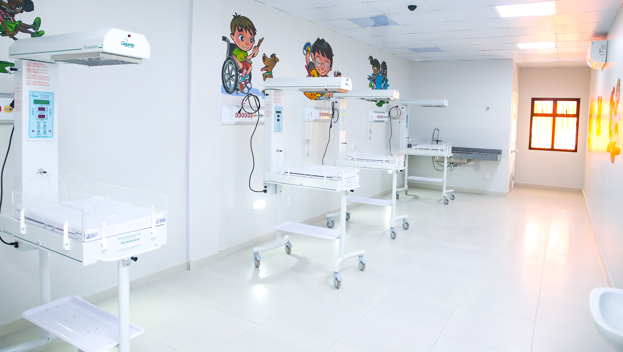 sala de hospital com pequenos leitos lado a lado e ilustrações infantis na parede
